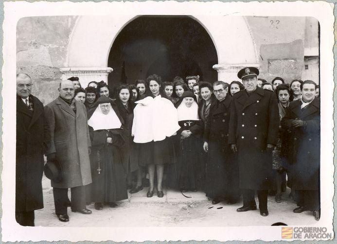 Divulgación. Asistencia sanitario-social. Bautizo. Tras la ceremonia, fotografía de los asistentes en la portada de un convento (sin identificar). Alcañiz